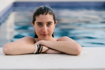 Portrait of wet teenage girl leaning at poolside