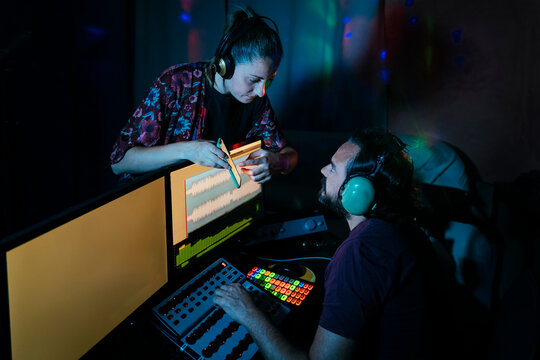 Woman Showing Smart Phone To Man Using Computer In Recording Studio At Home