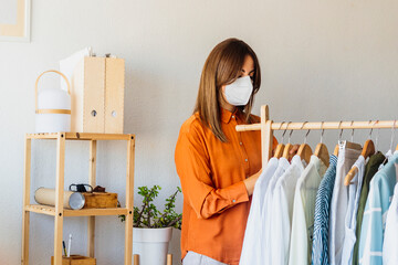 Female fashion designer working at home with clothes stand wearing protective face mask