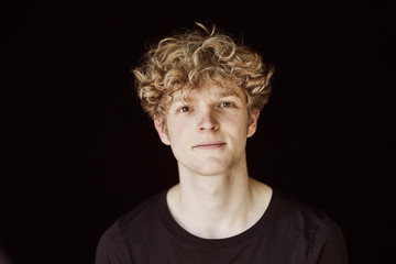 Portrait of young man with curly blond hair against black background