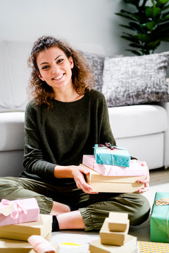 Portrait of smiling young woman sitting on the floor at home with wrapped presents