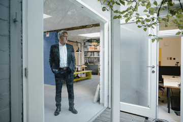 Senior businessman standing in office door looking outdoors with hands in pockets