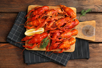 Delicious boiled crayfishes with lemon and dill on wooden table, top view