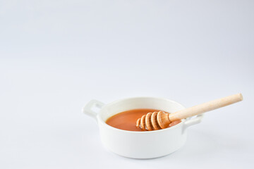 A bowl of liquid honey and a wooden spoon on a white background. Minimalism.