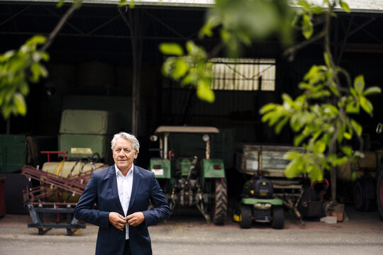 Senior businessman on a farm with tractor in barn
