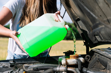 Midsection of woman on road trip pouring coolant in engine during sunny day