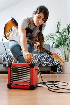Woman adjusting knobs on amplifier while playing electric guitar at home