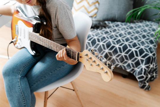 Woman playing electric guitar while sitting on chair at home