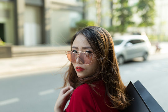 Close-up of confident woman wearing sunglasses carrying shopping bag on street in city