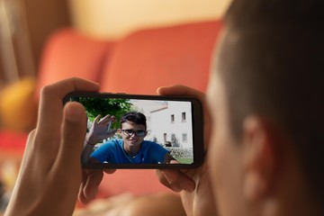 videoconference of two young people made by the mobile one lying on the couch at home and another young man in the middle of nature