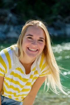 Smiling young woman with blond hair standing against river