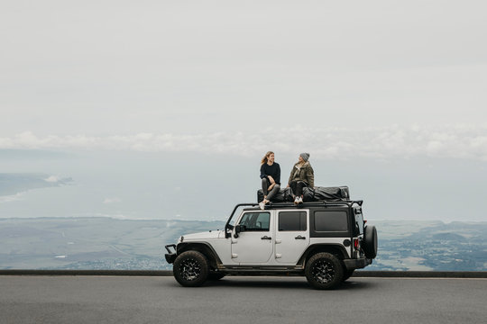 Friends talking while sitting on top of SUV at Maui, Hawaii, USA