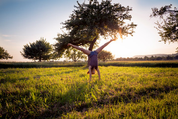 Teenage girl doing handstand in grassy field at sunset