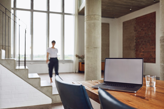 Laptop on wooden table in a loft flat with woman in background