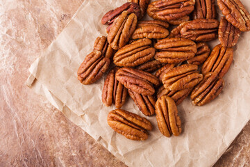 Scattering of pecans on paper, brown background, close up.