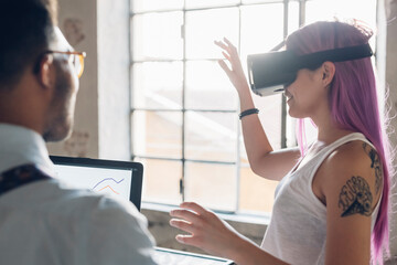 Two creative business people with VR goggles and laptop in loft office