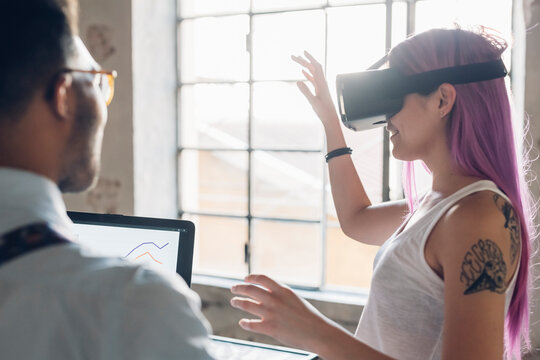 Two creative business people with VR goggles and laptop in loft office
