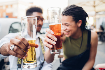 Happy young couple clinking beer glasses outdoors at a bar