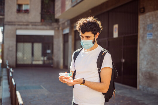 Young Man Wearing Mask Washing Hands With Sanitizer While Standing Against Building