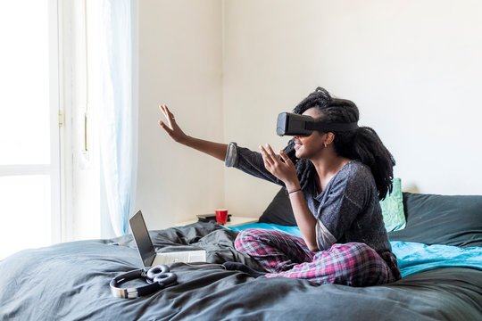 Young Woman Using Virtual Reality Glasses Sitting On Bed