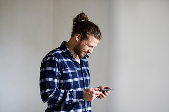 Smiling young man wearing checked shirt using smartphone - Powered by Adobe