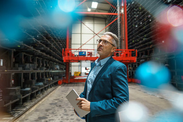 Mature businessman holding tablet in a high rack warehouse of a factory