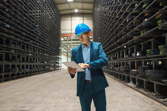 Mature businessman using tablet in a high rack warehouse of a factory
