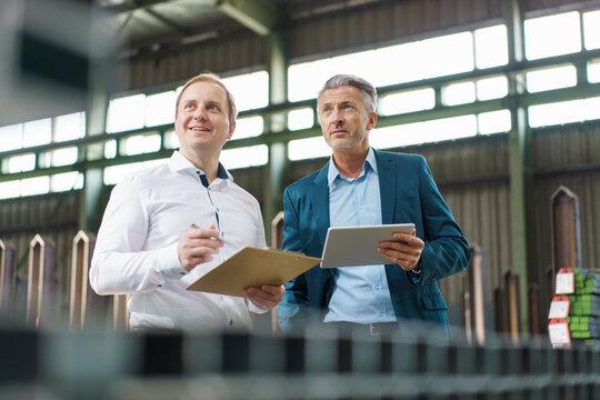 Two businessmen with tablet and clipboard having a meeting in a factory