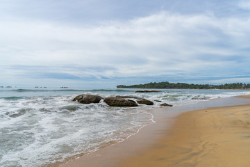 Fototapeta na wymiar Tropical beach with rocks in the sea. palm trees on the background. cloudy sky. Arugam bay, Sri Lanka
