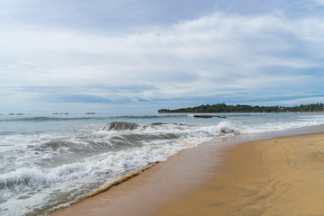 Fototapeta na wymiar Tropical beach with rocks in the sea. palm trees on the background. cloudy sky. Arugam bay, Sri Lanka