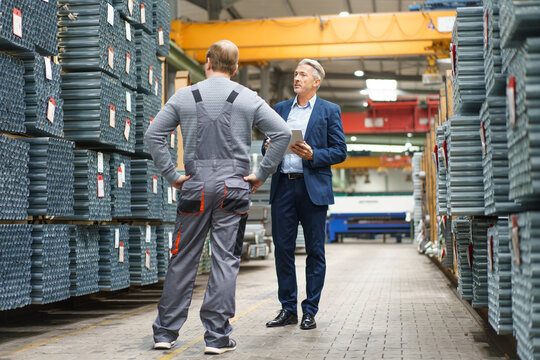 Businessman and worker talking in a factory storehouse