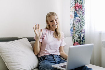 Smiling millennial woman sit on couch at home talk on video call with relatives, happy young female have Webcam conversation, take online course indoors