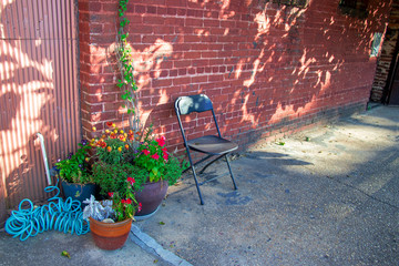 Plants and flowers in large ceramic pots and a single plastic folding chair against an old brick and tin wall make colorful industrial chic statement, with copy space.