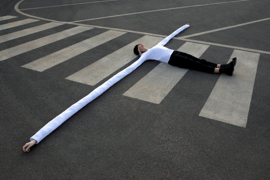 Woman with long artificial hands lying on crosswalk