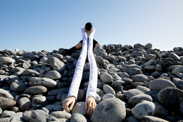 Woman with artificial long hands sitting on pebbles against clear sky