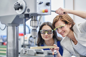 Female manager drilling metal while training worker in metal industry