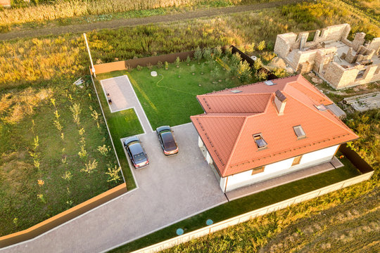Top down aerial view of two private houses, one under construction with concrete foundament and brick walls and another finished with red tiled roof.