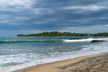 Tropical beach with waves and palm trees. cloudy sky. Arugam bay, Sri Lanka