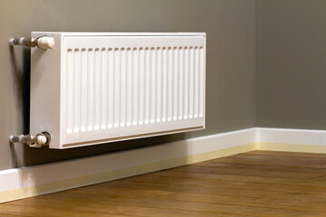 White metal heating radiator mounted on gray wall inside a room.