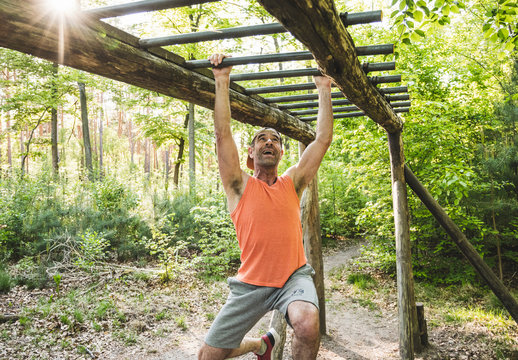 Happy man hanging from monkey bars while exercising at park