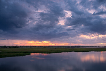 Storm clouds over the water with the sunset over the lake. Orange sunlight, dramatic sky with clouds. Beautiful reflections in water