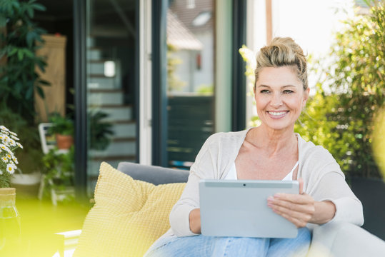Portrait of happy mature woman sitting on terrace with digital tablet