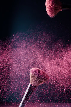 Make-up brush with violet powder explosion on black background
