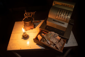 cash register, coffee grinder and old money lit by the flame of an old lamp on wooden table, 