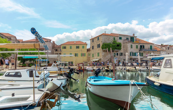 Beautiful waterfront view of a small town of Postira on the island of Brac in Croatia. Old wooden boats docked in the ancient harbour, bright colorful warm summer day, stone houses in the area