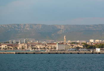 Fototapeta na wymiar View of Split, Croatia town from a car ferry approaching for very far. Church belltower seen rising above the old buildings, mountains and sky in the distance