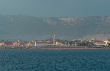 Fototapeta premium View of Split, Croatia town from a car ferry approaching for very far. Church belltower seen rising above the old buildings, mountains and sky in the distance