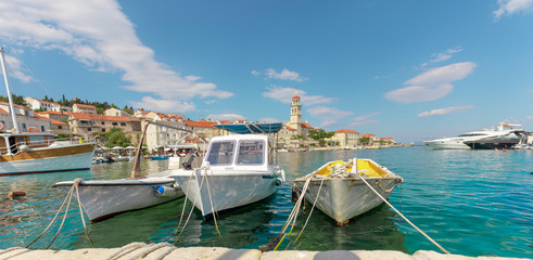 Fototapeta na wymiar Beautiful picturesque waterfront view of a small town of Sutivan on the island of Brac. Old boats docked in the harbour, belltower seen in the distance on a warm blue summer day