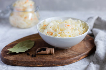 Fermented homemade sauerkraut in a white bowl on a wooden stand against a light background. Home preparations, canning. The best prebiotic