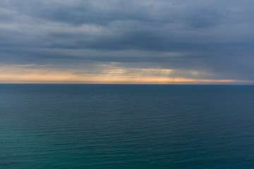 Sea horizon with rays and storm clouds. Calm sea background. Bright blue water and grey rain clouds.